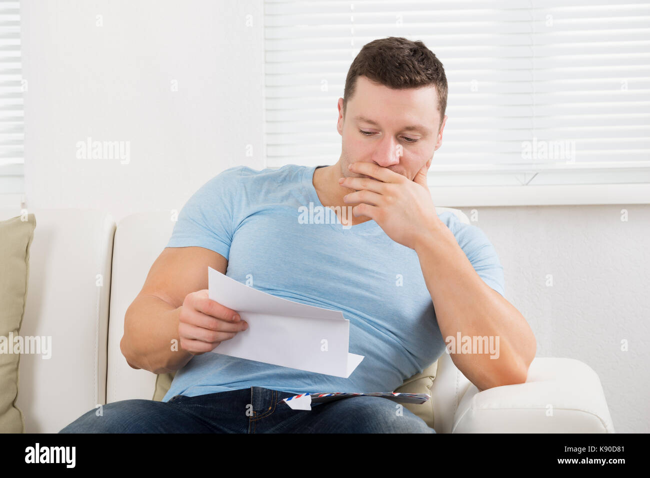 De graves Mid adult man reading lettre sur canapé à la maison Banque D'Images