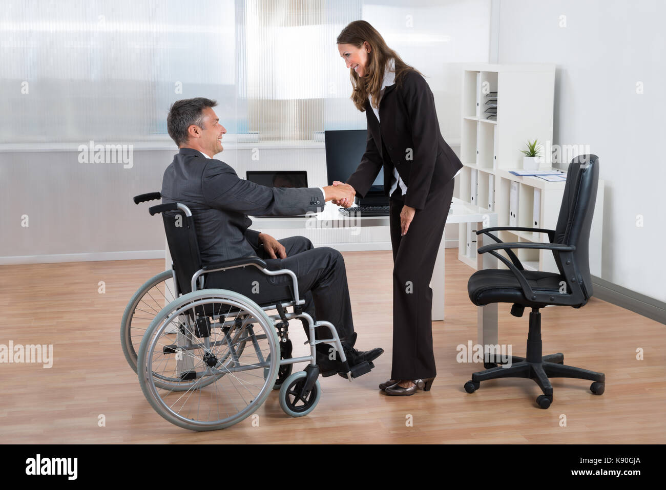 Happy businesswoman shaking hands with businessman sur fauteuil roulant dans office Banque D'Images
