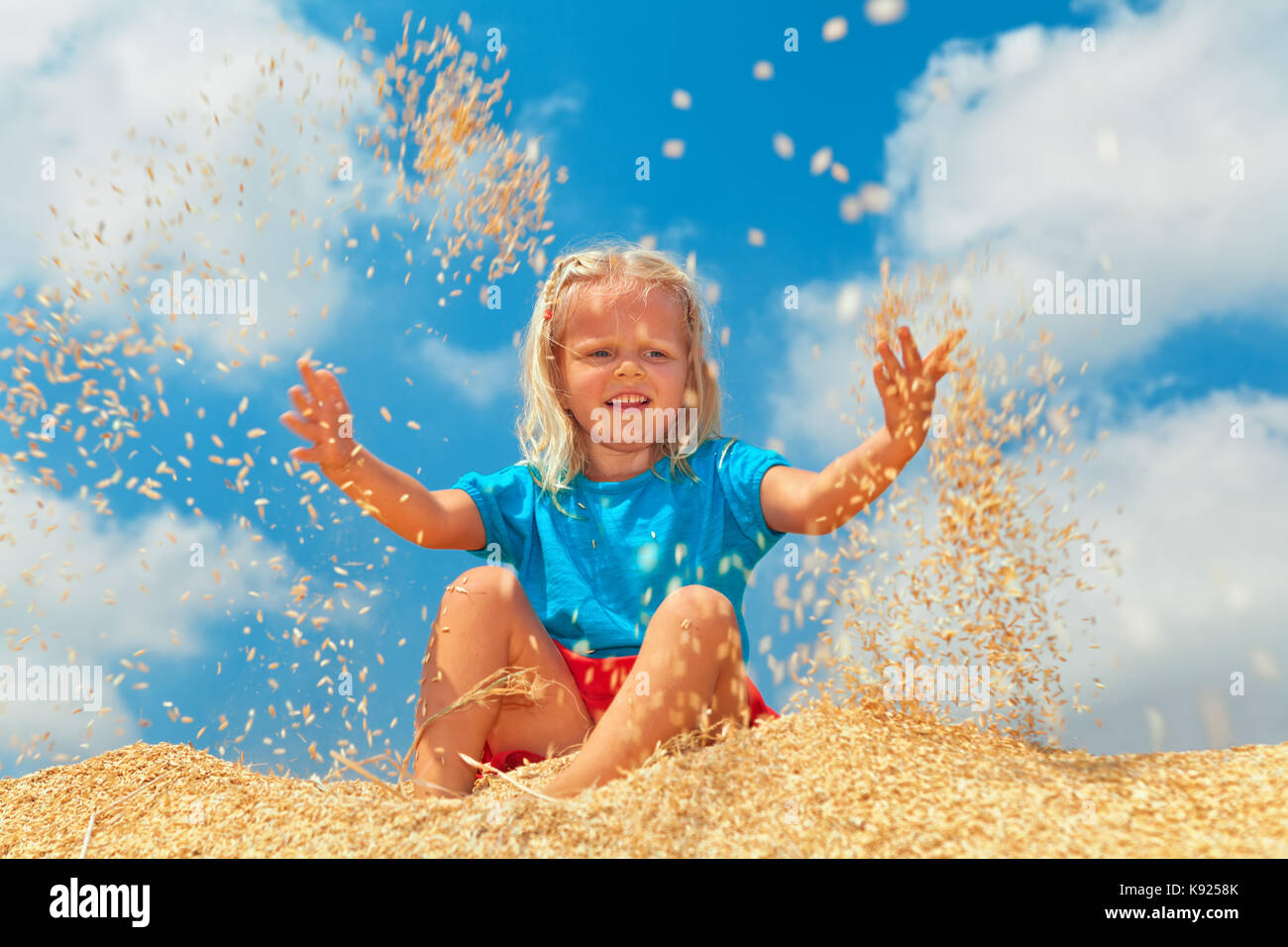 Pays de la famille vacances avec les enfants la plantation. bonne enfant s'asseoir sur le tas de récolte des céréales de la ferme. petit fermier à vomir dans les semences de riz fraîche de l'air. Banque D'Images