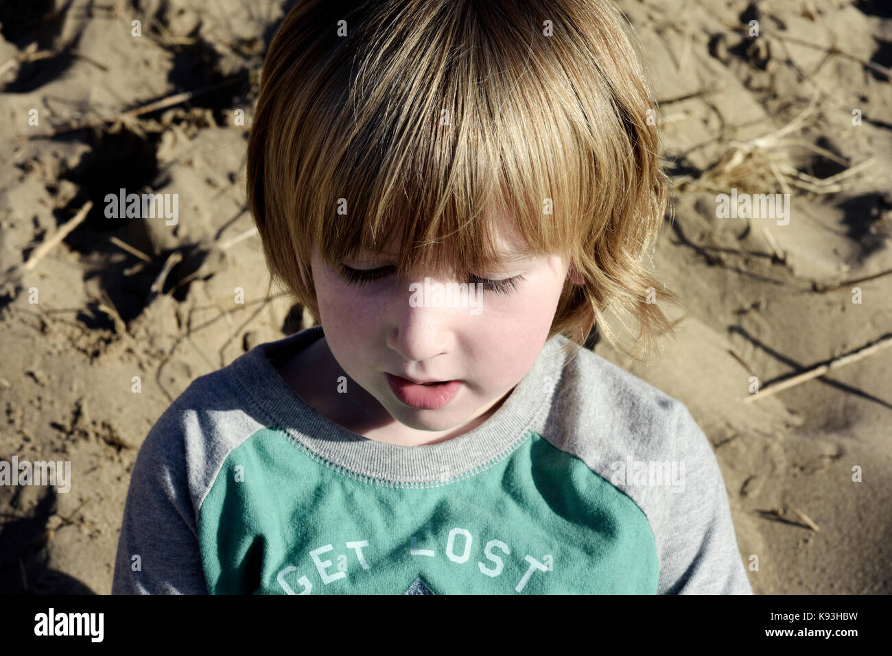 Un jeune garçon est assis sur les dunes de sable sur une plage whils il contemple la vie. Banque D'Images