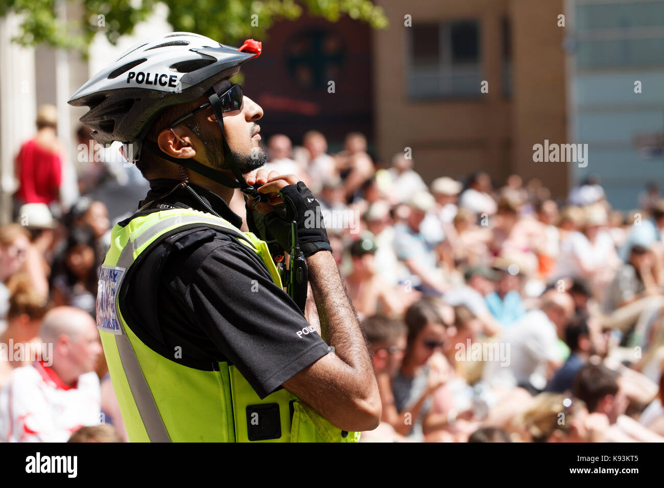Un policier britannique asiatique ajuste son casque de vélo pédale devant une grande foule a un événement dans le centre de Birmingham, UK Banque D'Images