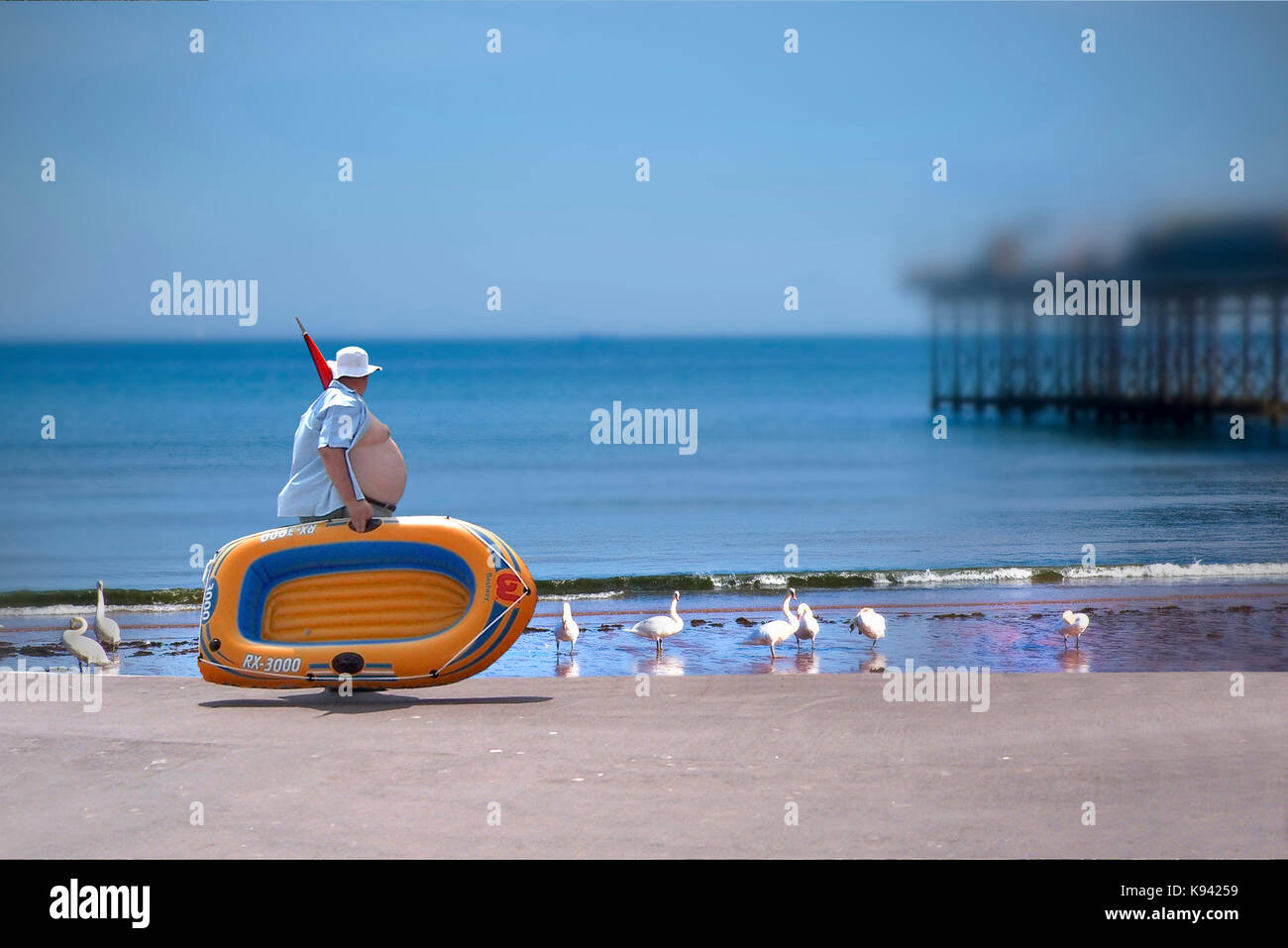 Image composite de l'excès de l'homme exerçant son bateau gonflable le long de la promenade du bord de mer à Torquay dans le devon avec cygnes de mer sur la plage et la jetée b/g Banque D'Images