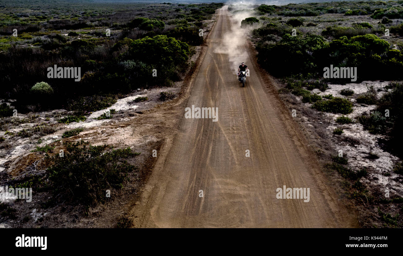 Paysage avec man riding moto cafe racer le long chemin de terre poussiéreux. Banque D'Images