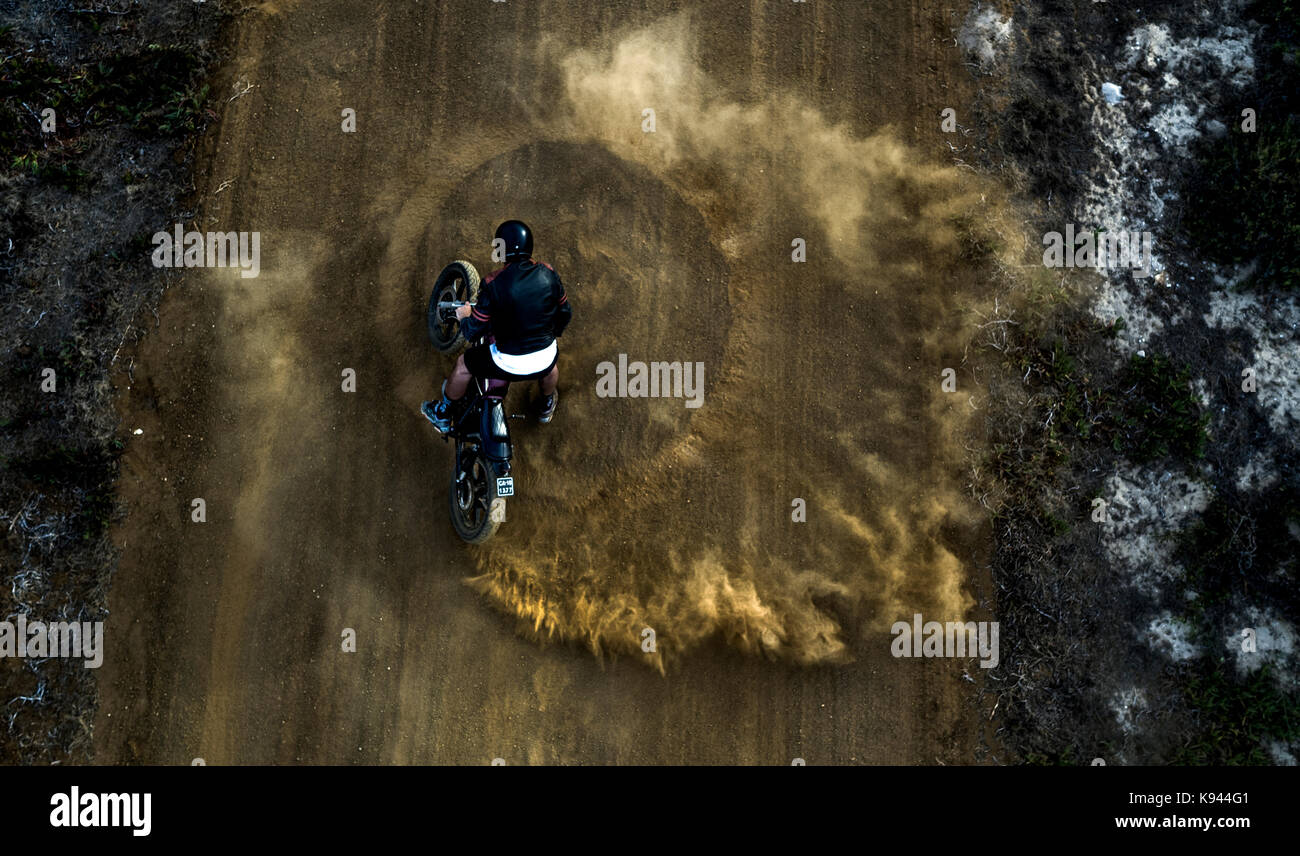 Portrait de l'homme conduisant cafe racer moto dans des cercles sur une route de terre poussiéreuse. Banque D'Images