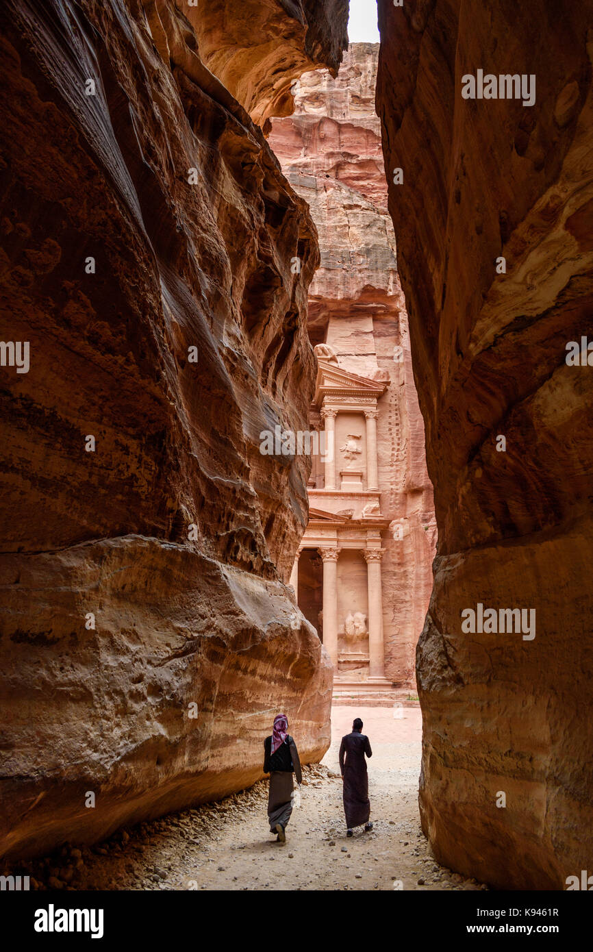 Deux personnes marchant à travers la formation rocheuse étroite vers les architecture de al khazneh ou le conseil du trésor à Pétra, en Jordanie. Banque D'Images