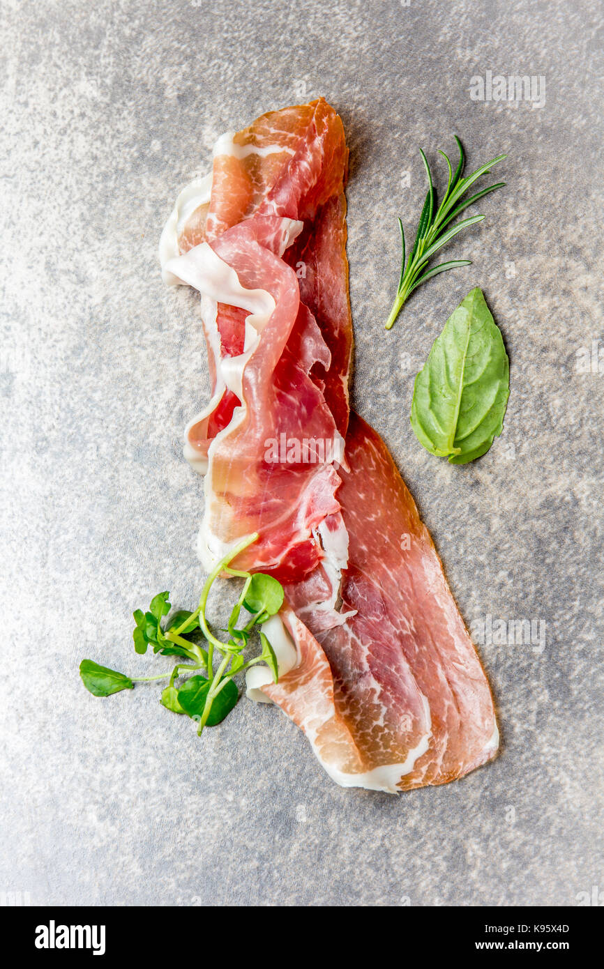 Arrière-plan de l'alimentation avec du jambon jamon serrano et d'aromates, romarin, basilic et salade de cresson, pierre fond gris, vue d'en haut. Banque D'Images