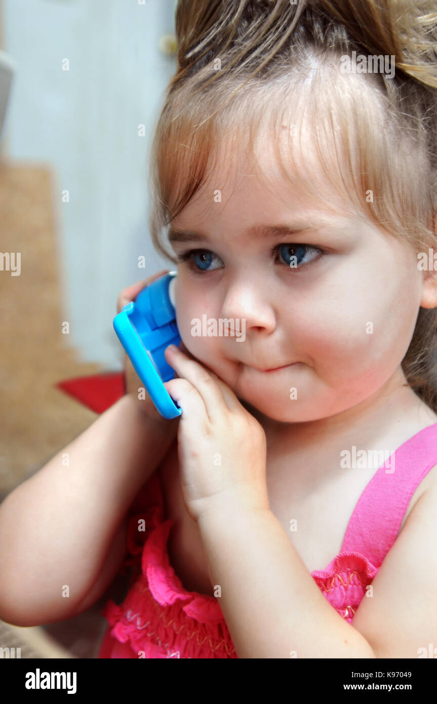 Adorable petite fille répond à son téléphone cellulaire et prétendre est fatigué d'être mis "en attente.' elle fait un drôle de visage comme elle tient le téléphone à son e Banque D'Images