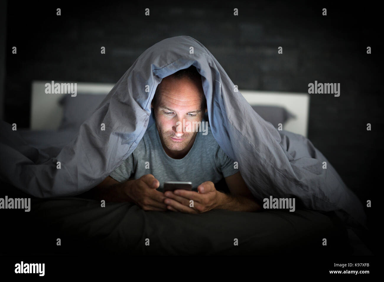 Jeune homme addict téléphone cellulaire éveillé tard dans la nuit dans le lit using smartphone Banque D'Images