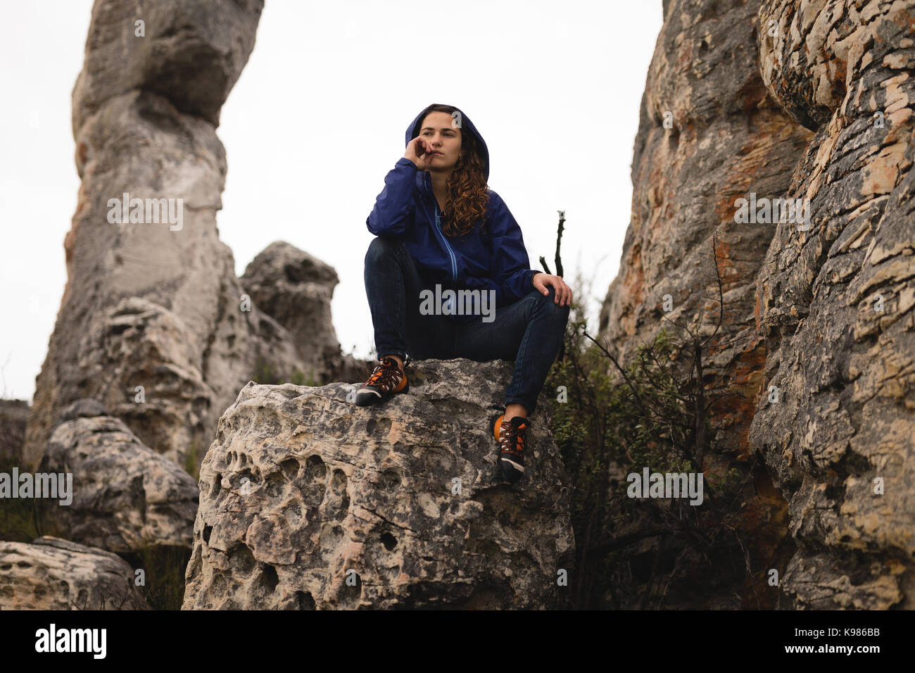 Thoughtful woman sitting on rock pendant l'alpinisme Banque D'Images