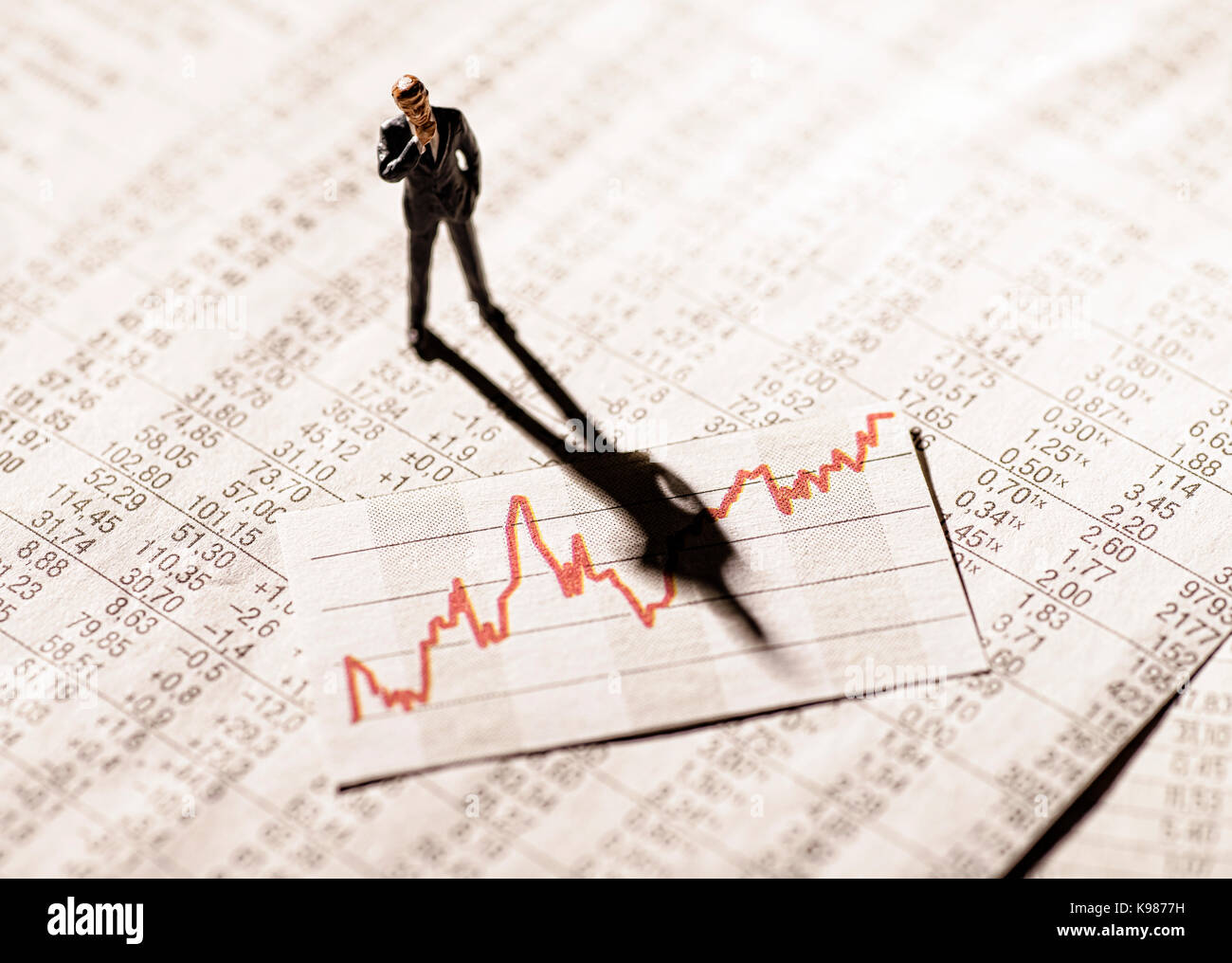 La figure de modèle se trouve sur des tables de taux et semble sceptique sur un graphique avec le prix des actions. Banque D'Images