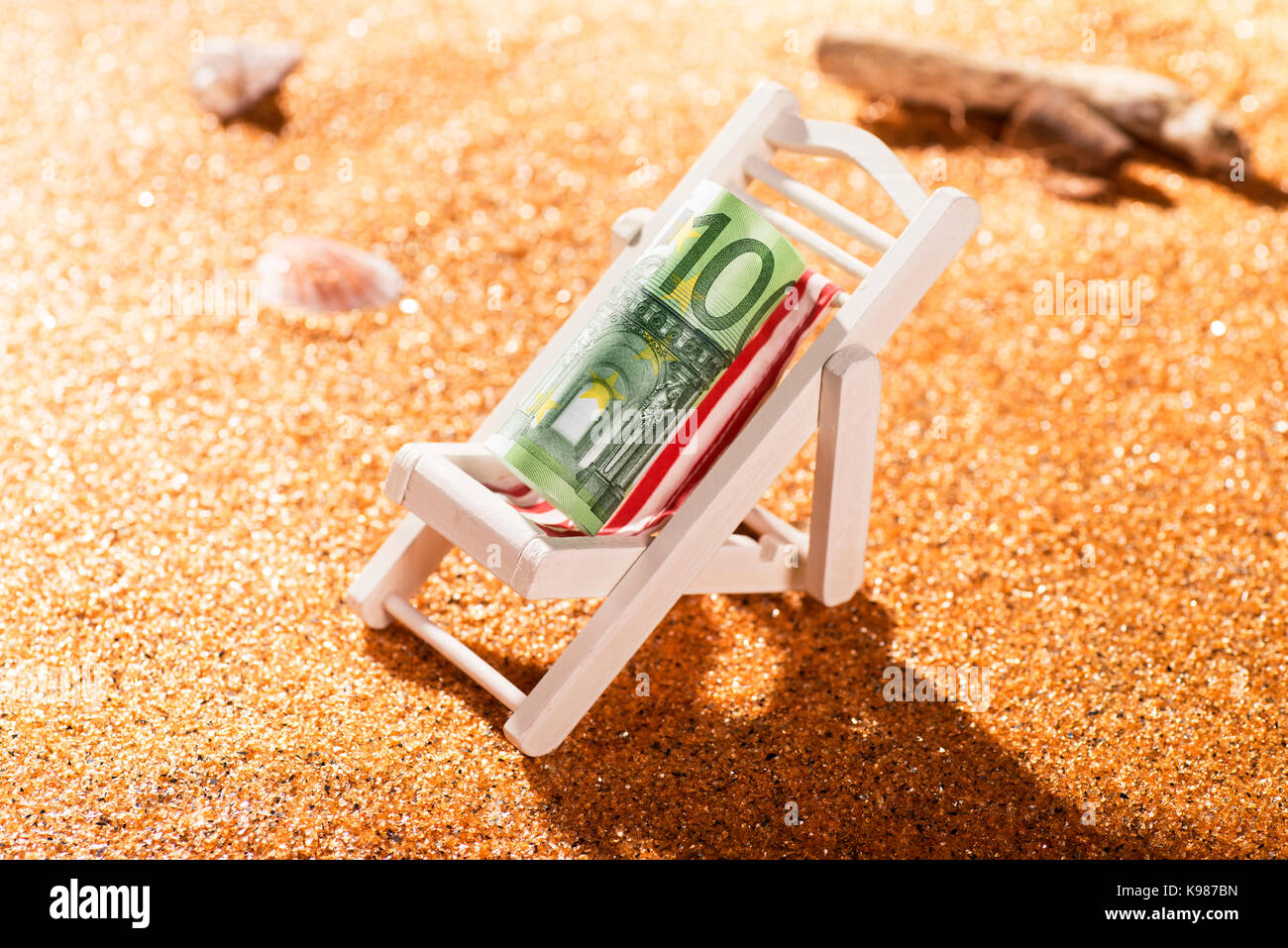 Un billet en euros 100 roulé sur une chaise longue dans une scène de plage Banque D'Images