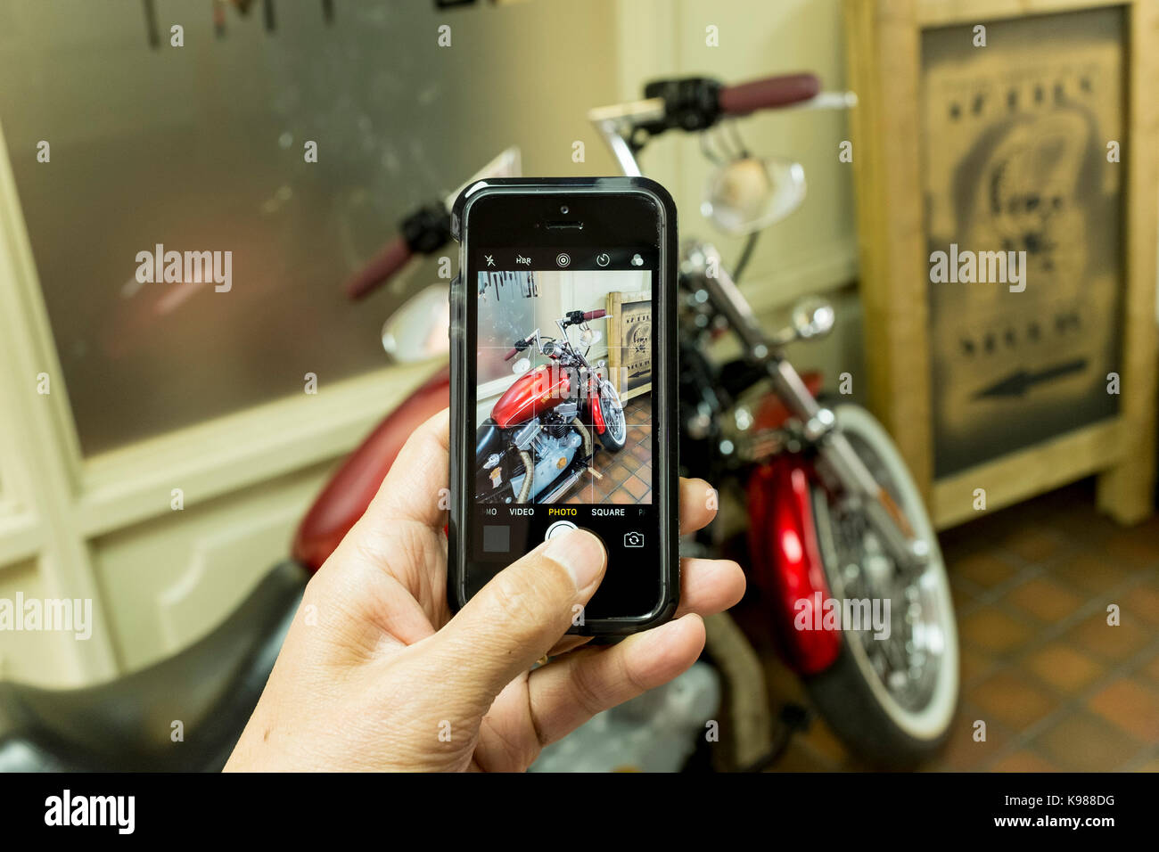 Un homme prenant photo d'une moto Harley Davidson rouge avec un iPhone smartphone SE Banque D'Images