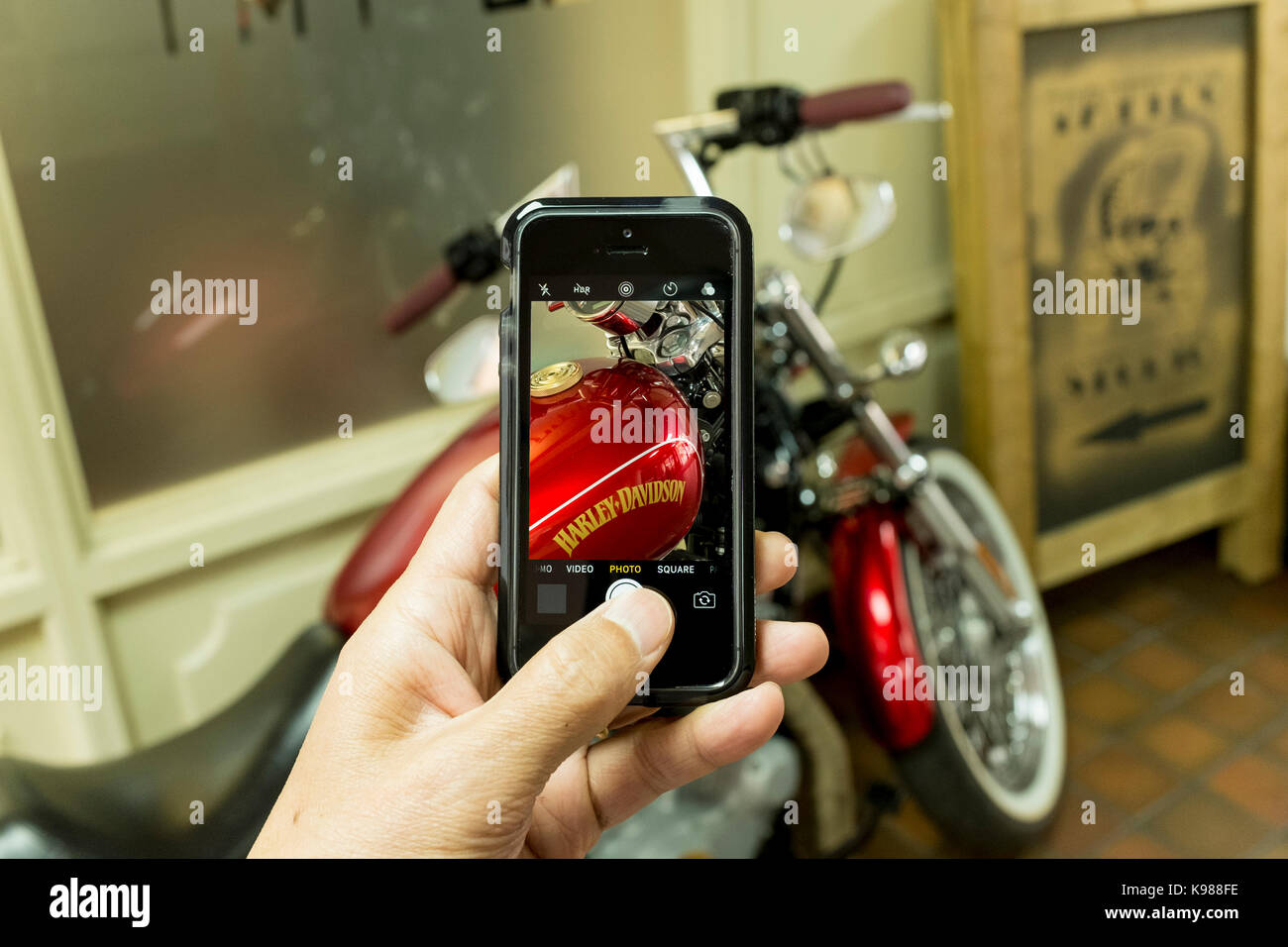 Un homme prenant photo d'une moto Harley Davidson rouge avec un iPhone smartphone SE Banque D'Images