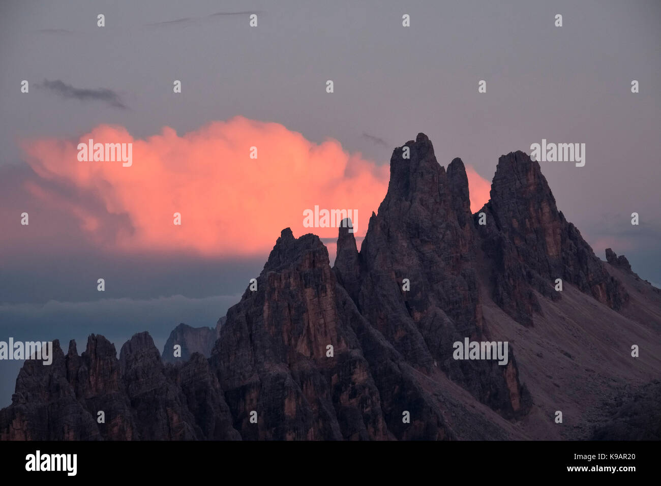 Les Dolomites, Italie du Nord. Les pics dentelés du dei crêpe Ronde (2182m) après le coucher du soleil, silhouetté contre un nuage rose Banque D'Images