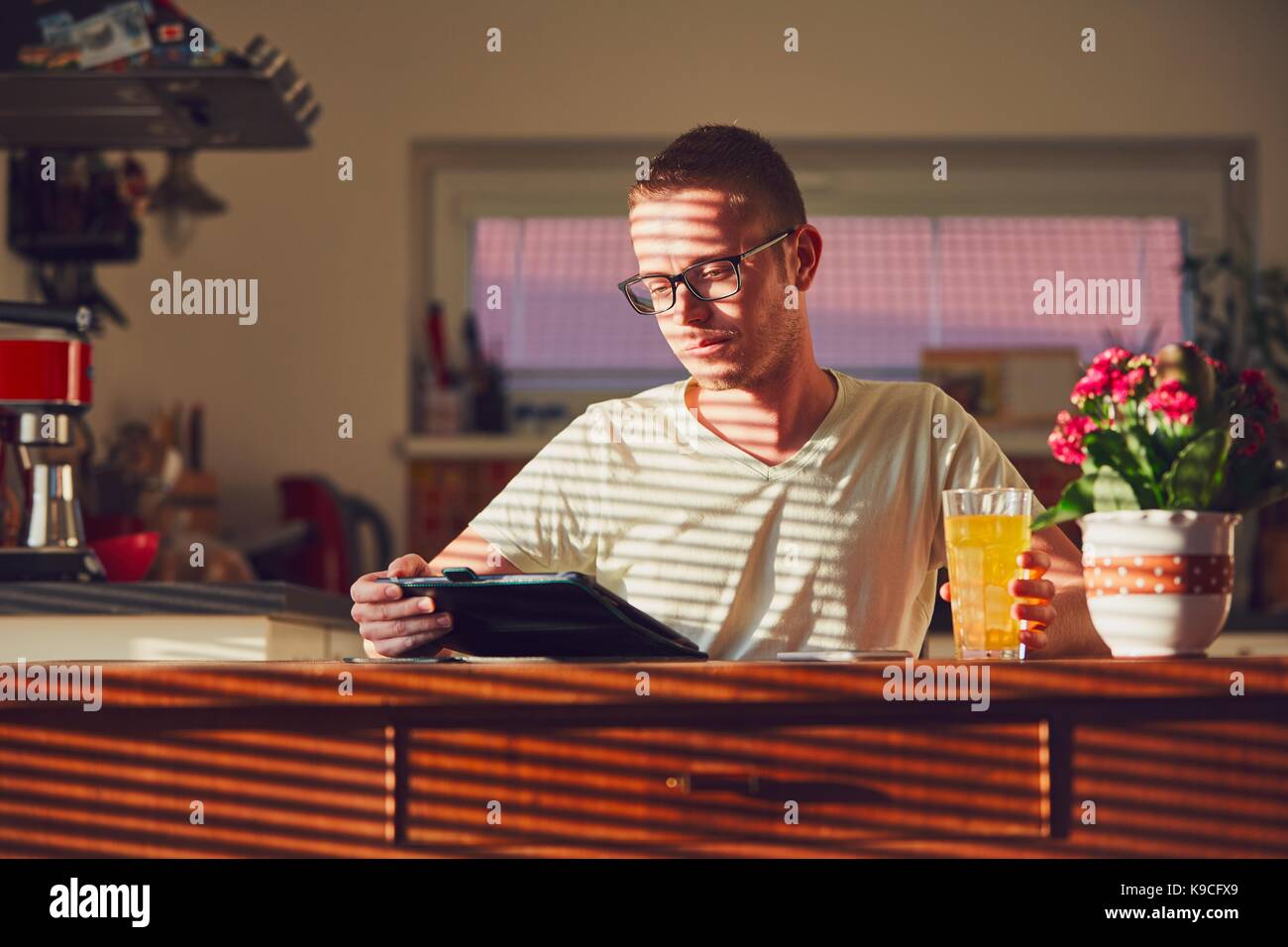 Matin de temps à la maison. Jeune homme lecture sur la tablette numérique dans la cuisine pendant le petit déjeuner. Banque D'Images
