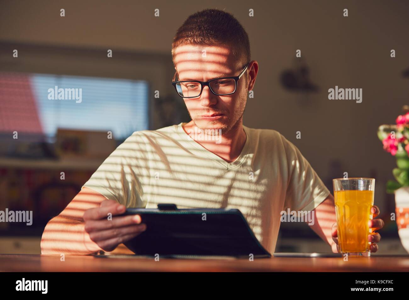 Matin de temps à la maison. Jeune homme lecture sur la tablette numérique dans la cuisine pendant le petit déjeuner. Banque D'Images