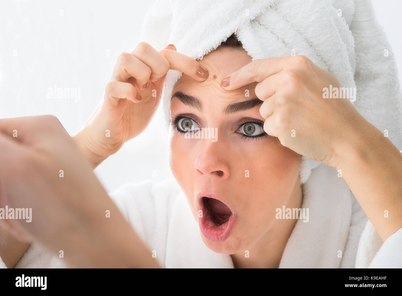 Choqué woman looking at bouton sur le front dans le miroir Banque D'Images