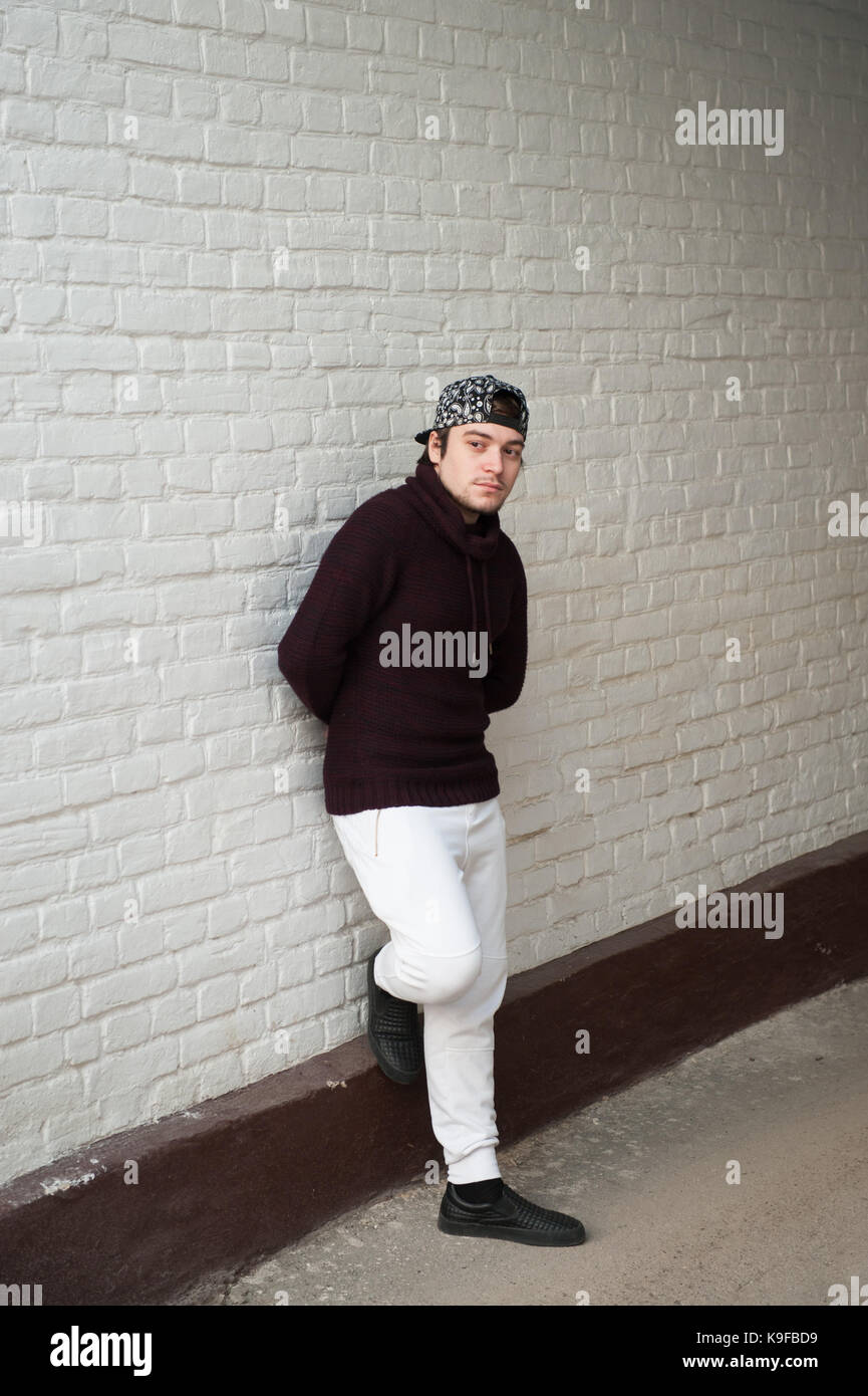 Beau jeune homme dans une casquette de baseball et chandail et pantalon  blanc sur un mur en brique blanche background Photo Stock - Alamy