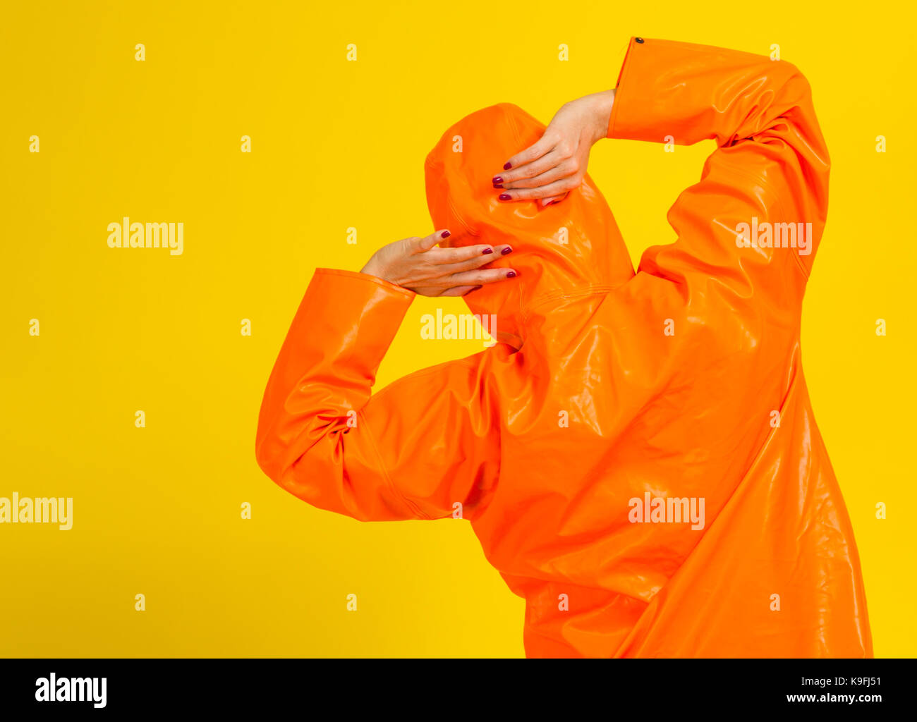 Vue arrière de jeune femme en vêtements de pluie orange sur fond jaune Banque D'Images