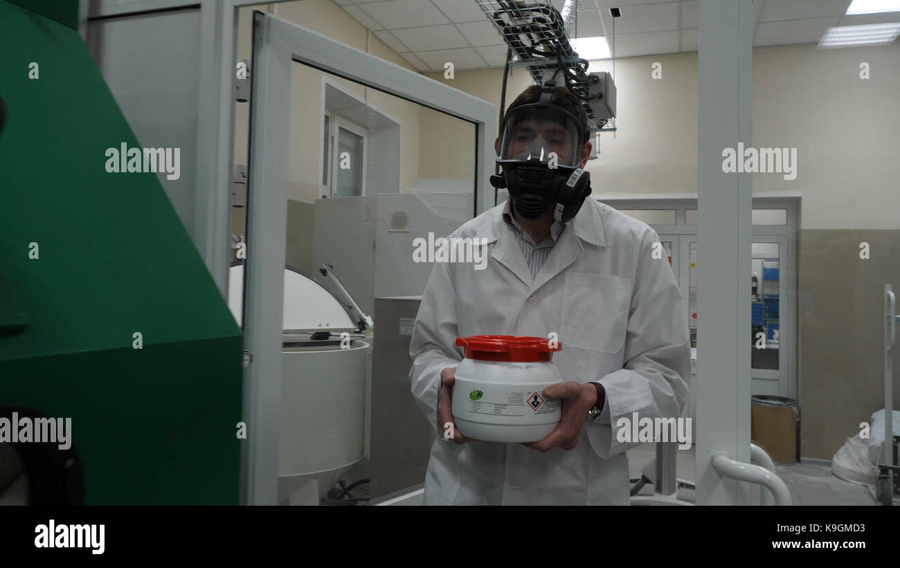 Porter des vêtements protecteurs et scientifique portant un pot de liquide toxique à l'intérieur d'une zone à risque biologique Banque D'Images