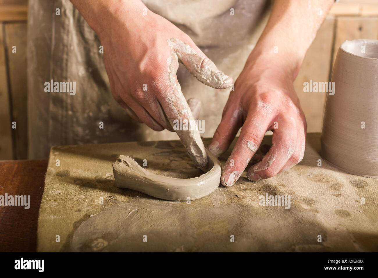 La poterie, grès, céramique art concept - gros plan sur la poignée formant les doigts artisan à partir de la matière argile réfractaire, maître mains travailler avec quelques morceau d'argile, homme stand à un atelier près de la table. Banque D'Images