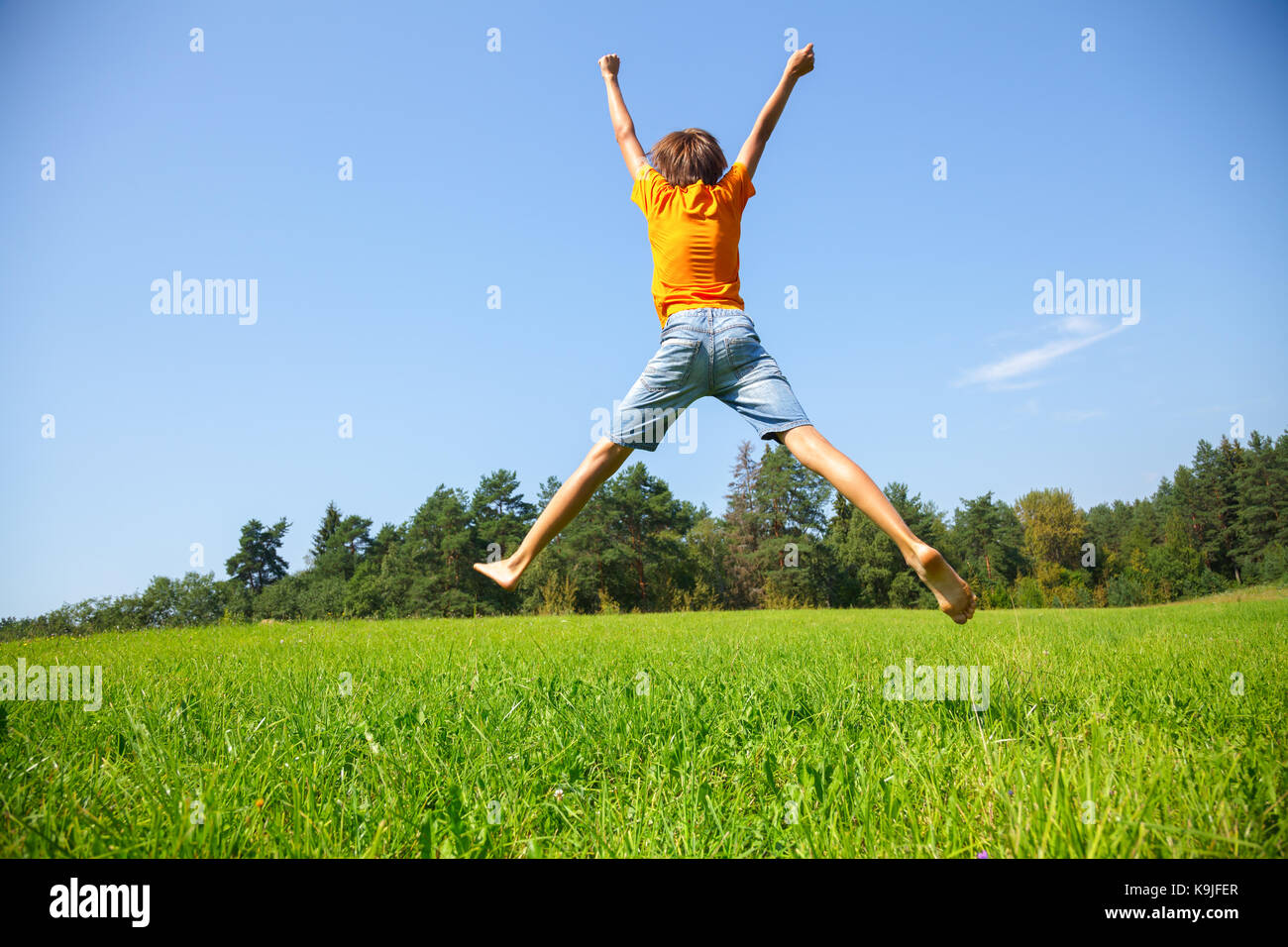 Kid jumping on the Sunny meadow en un été Banque D'Images