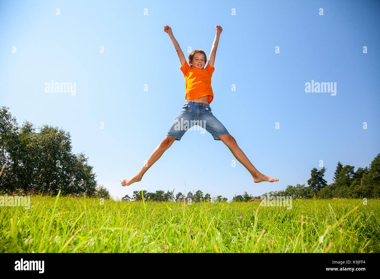 Kid jumping on the Sunny meadow dans une forêt d'été Banque D'Images