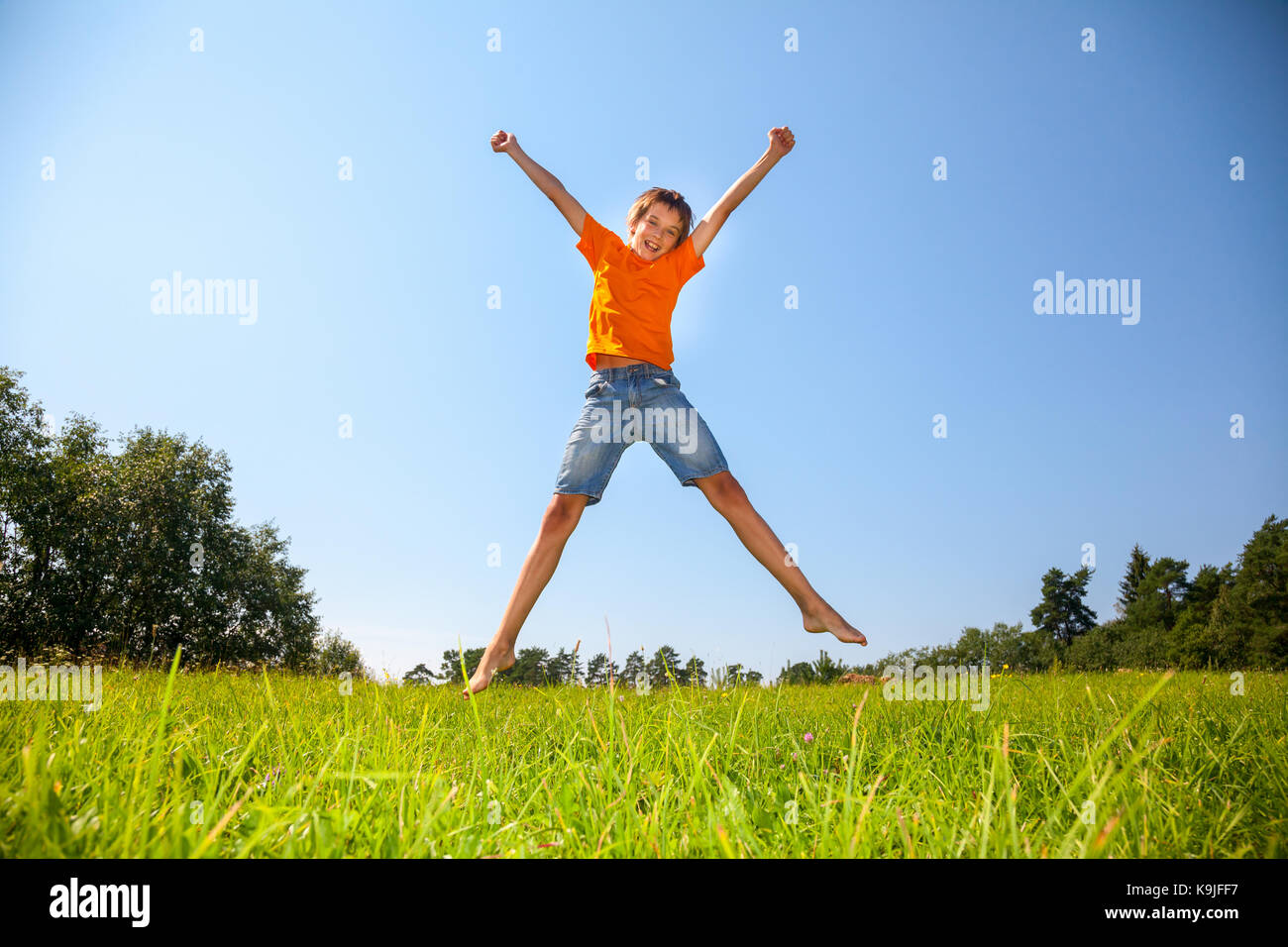 Bénéficiant d'été garçon sautant sur le sunny meadow dans une forêt d'été Banque D'Images