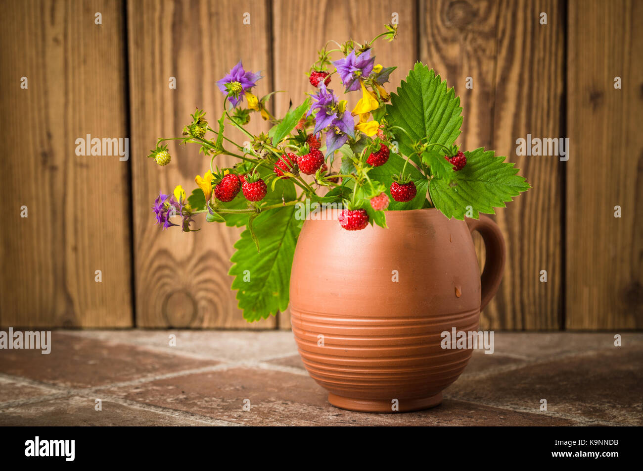 Fraise mûre et un bouquet de fleurs de la forêt dans une tasse d'argile Banque D'Images