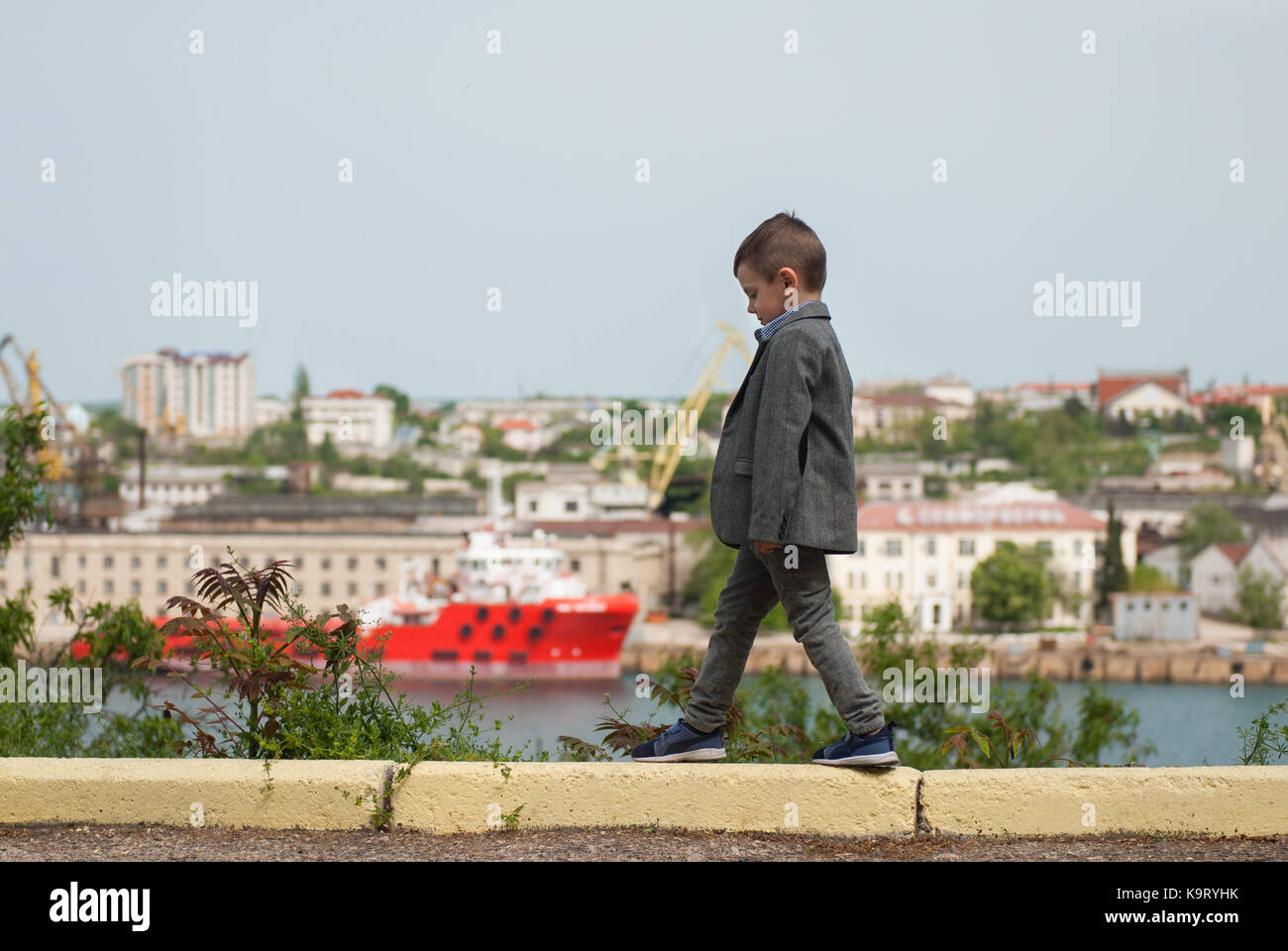 Heureux petit garçon veste en marchant sur le trottoir à l'arrière-plan de la mer port Banque D'Images