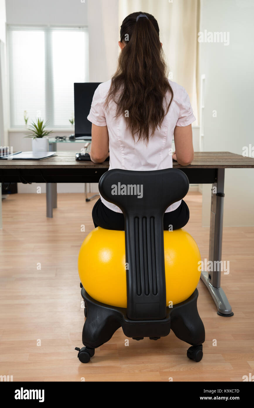 Young businesswoman sitting on fitness ball tout en travaillant sur computer in office Banque D'Images