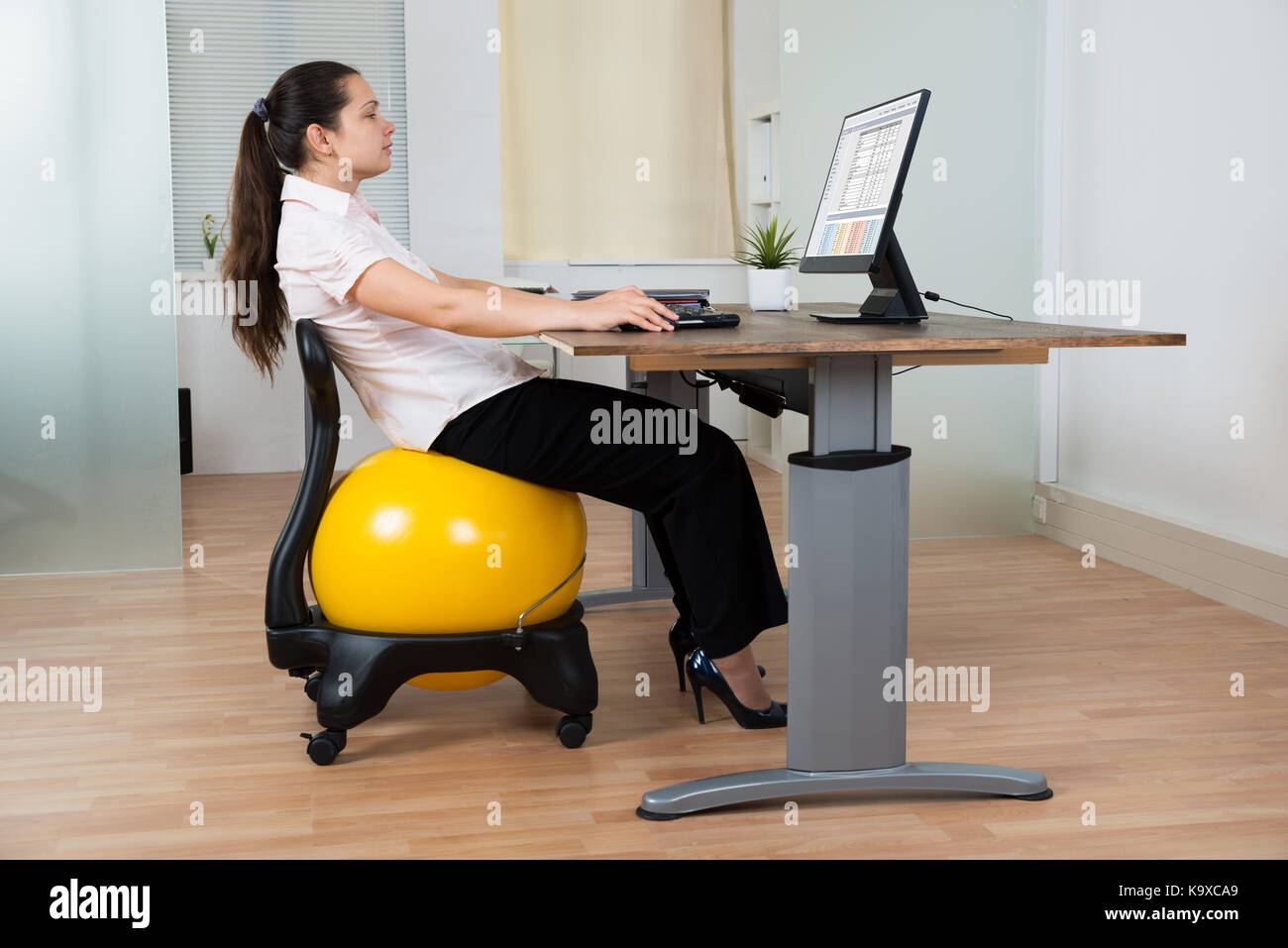 Businesswoman leaning on chair avec fitness ball tout en travaillant sur l'ordinateur Banque D'Images
