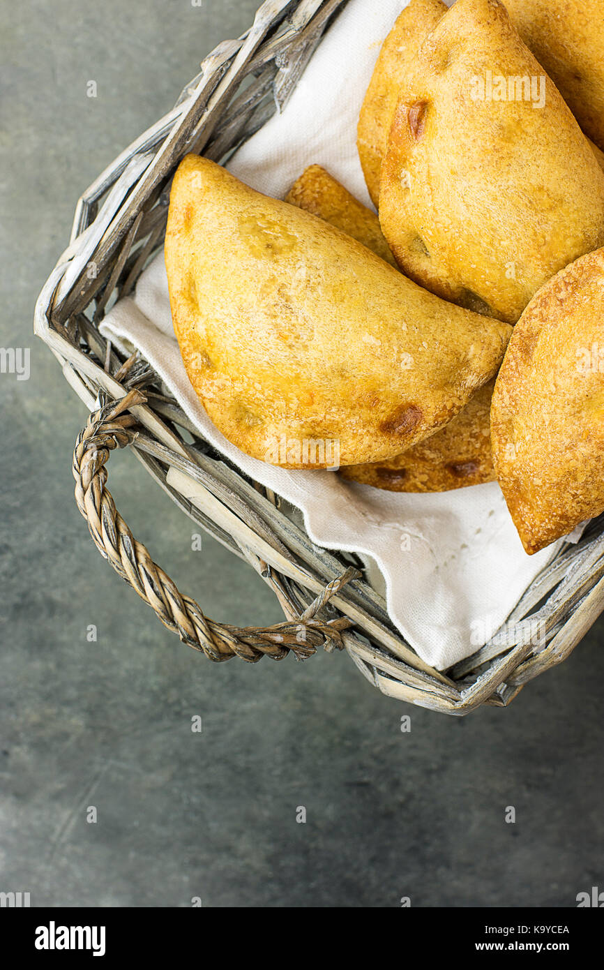 Des empanadas fraîchement cuits au four avec légumes tartes roulement pisto de fromage en sauce tomate dans panier en osier foncé. pâtisserie espagnol. sto en béton Banque D'Images