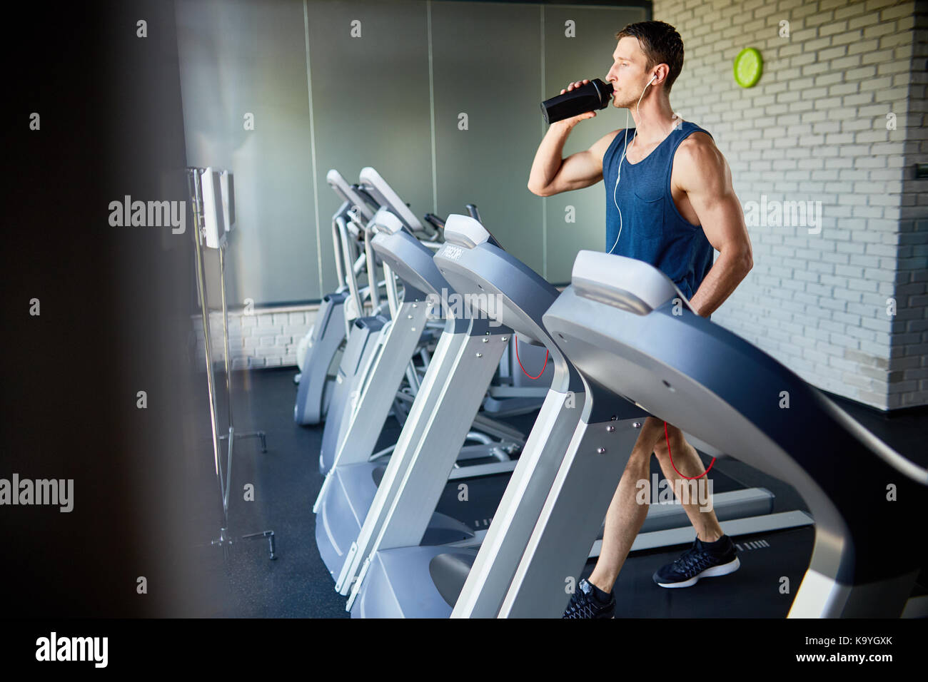 Young sportsman dans les écouteurs l'eau potable de la bouteille tout en  courant sur tapis roulant dans une salle de sport moderne, vue de profil  Photo Stock - Alamy