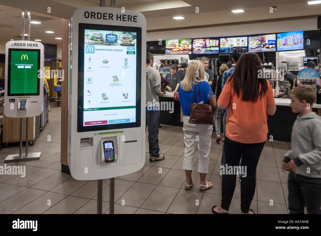 Les clients à l'intérieur d'une file d'un restaurant Mcdonald's, ignorant les nouvelles bornes libre-service. Stratford Upon Avon, Warwickshire, England, GB, au Royaume-Uni. Banque D'Images