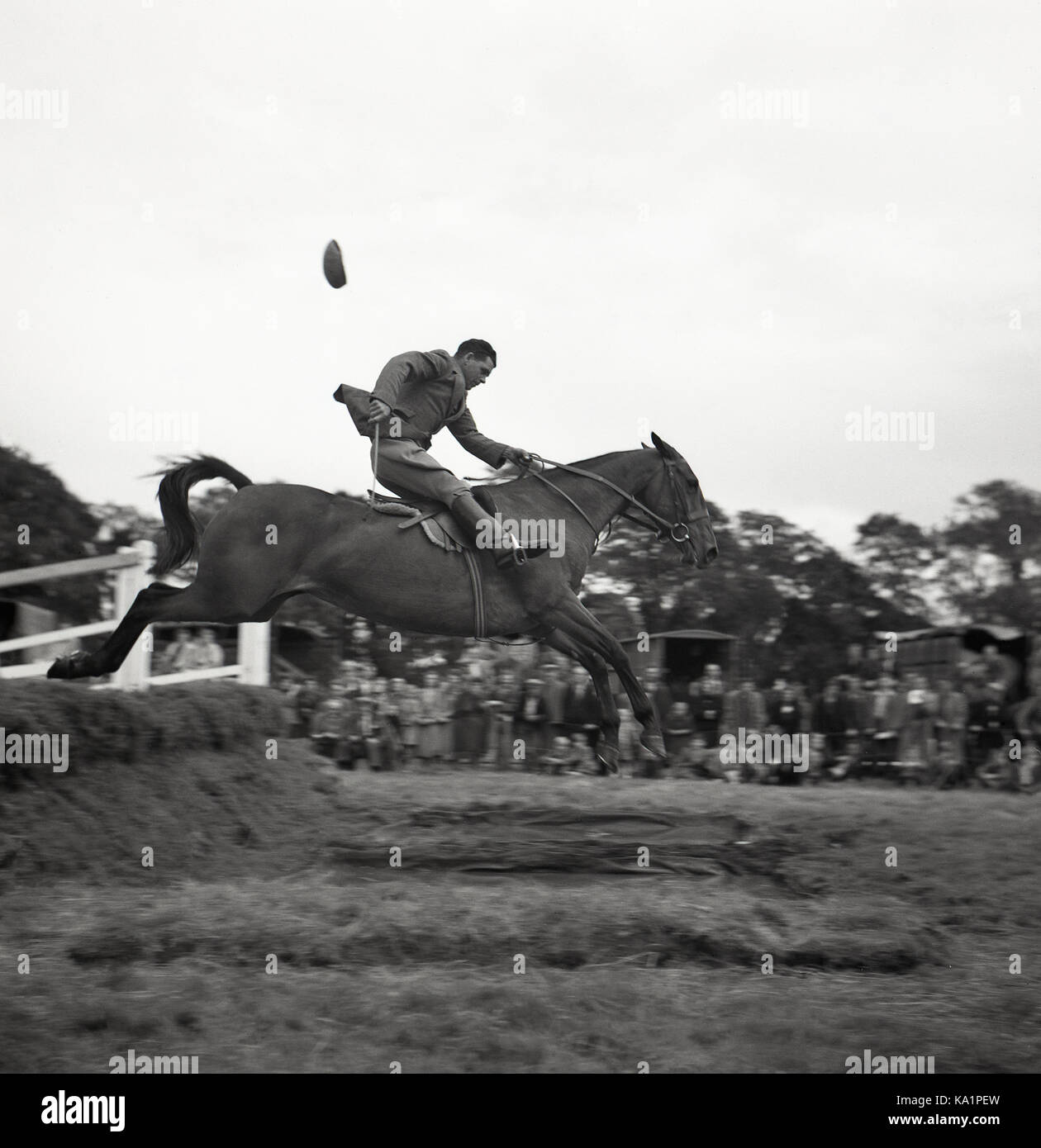 Années 1950, compétition historique en plein air, un cavalier sur son cheval sautant au-dessus d'un danger d'eau, tenant les rênes du cheval d'une main tandis que sa casquette en tissu vole, Irlande du Nord. Banque D'Images