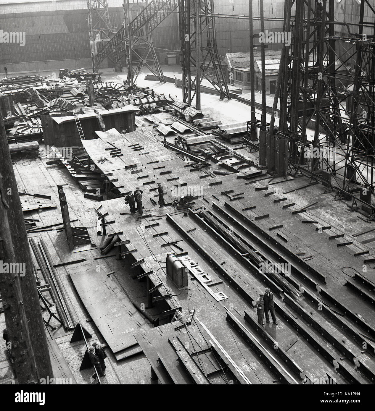 Début des années 1950, photo historique de J Allan Cash montrant des ouvriers sur le terrain, éclipsé par les gantries géantes du chantier naval de Harland & Wolff sur les quais de Belfast, en Irlande du Nord, célèbre pour le site où le Titantic Ocean Liner a été construit. Banque D'Images
