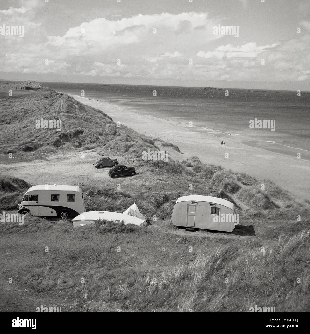 Années 1950, historique, une fourgonnette et caravane de l'époque garée sur des dunes de sable sur une longue plage de sable et la côte, Antrim, Irlande du Nord. Banque D'Images