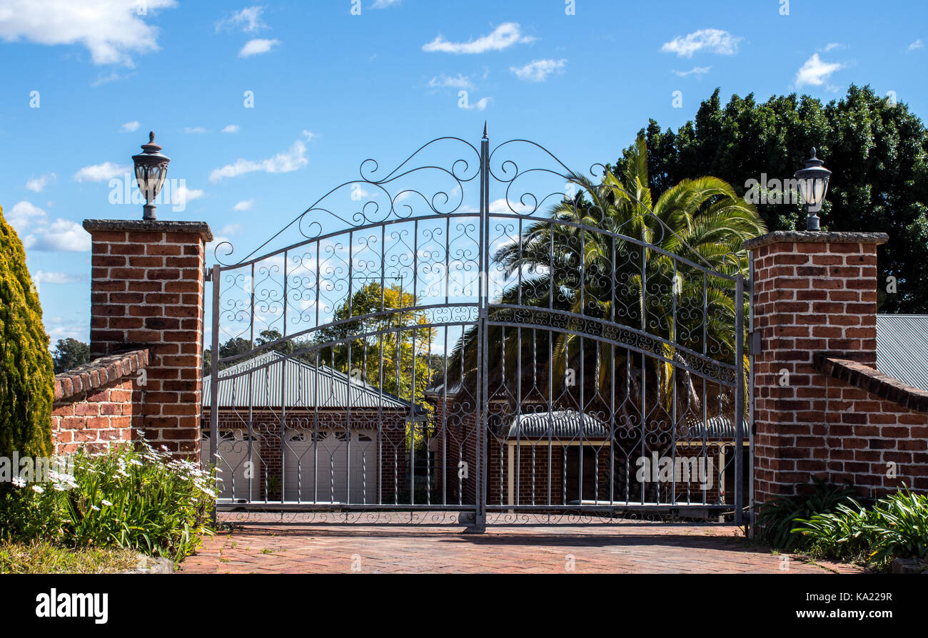 L'entrée des portes d'entrée de sécurité en métal situé dans quartier résidentiel avec jardin clôture en brique en arrière-plan contre le ciel bleu Banque D'Images