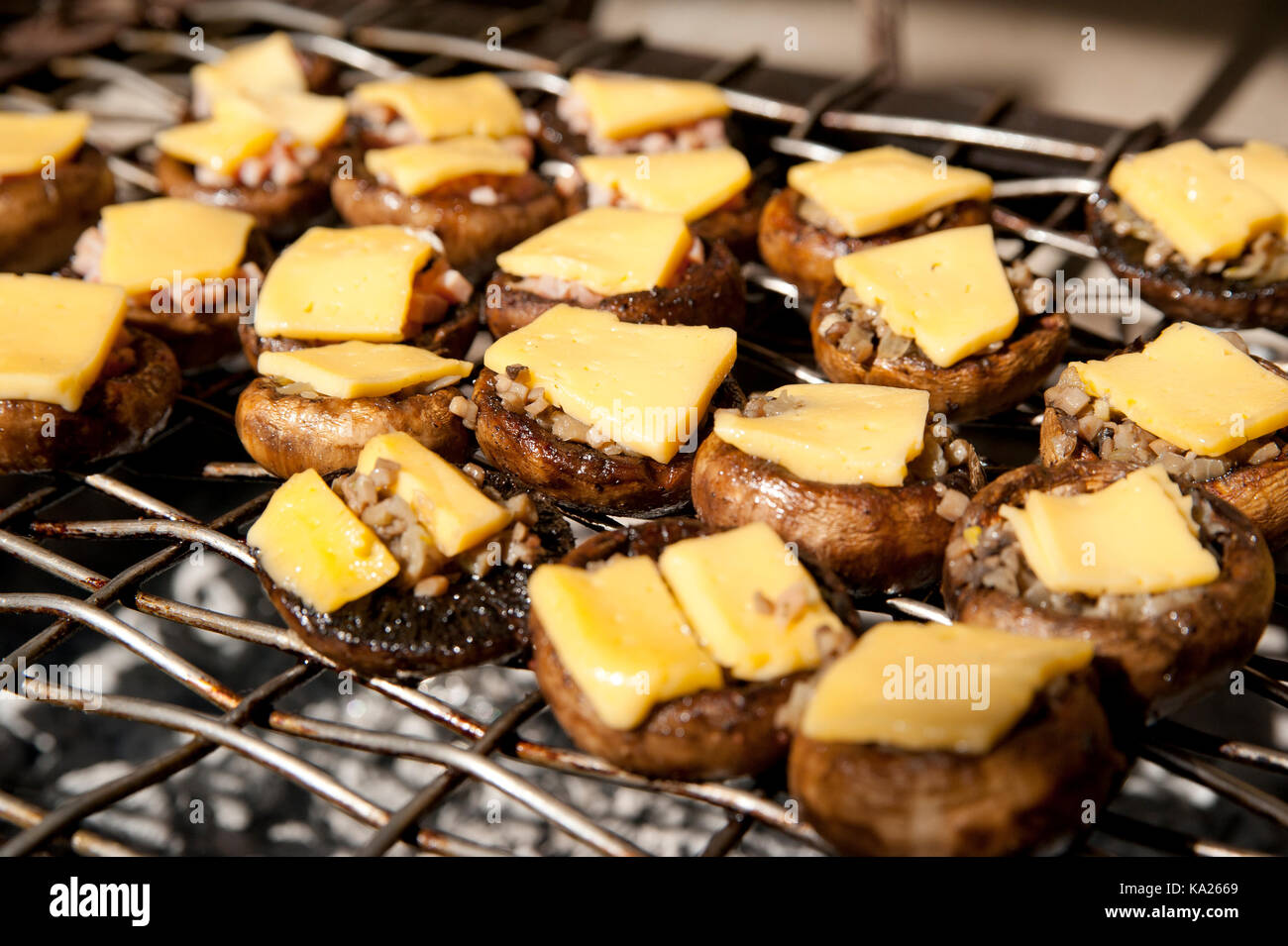 D'un bouton caps mashroom (champignons portobello) avec des tranches de fromage sur un haut, sur une grille de cuisson Banque D'Images