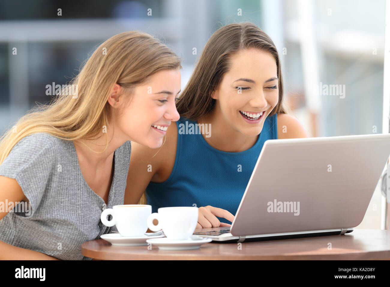 Heureux deux amis qui rient en regardant à la ligne du contenu dans un ordinateur portable assis sur une terrasse de restaurant Banque D'Images