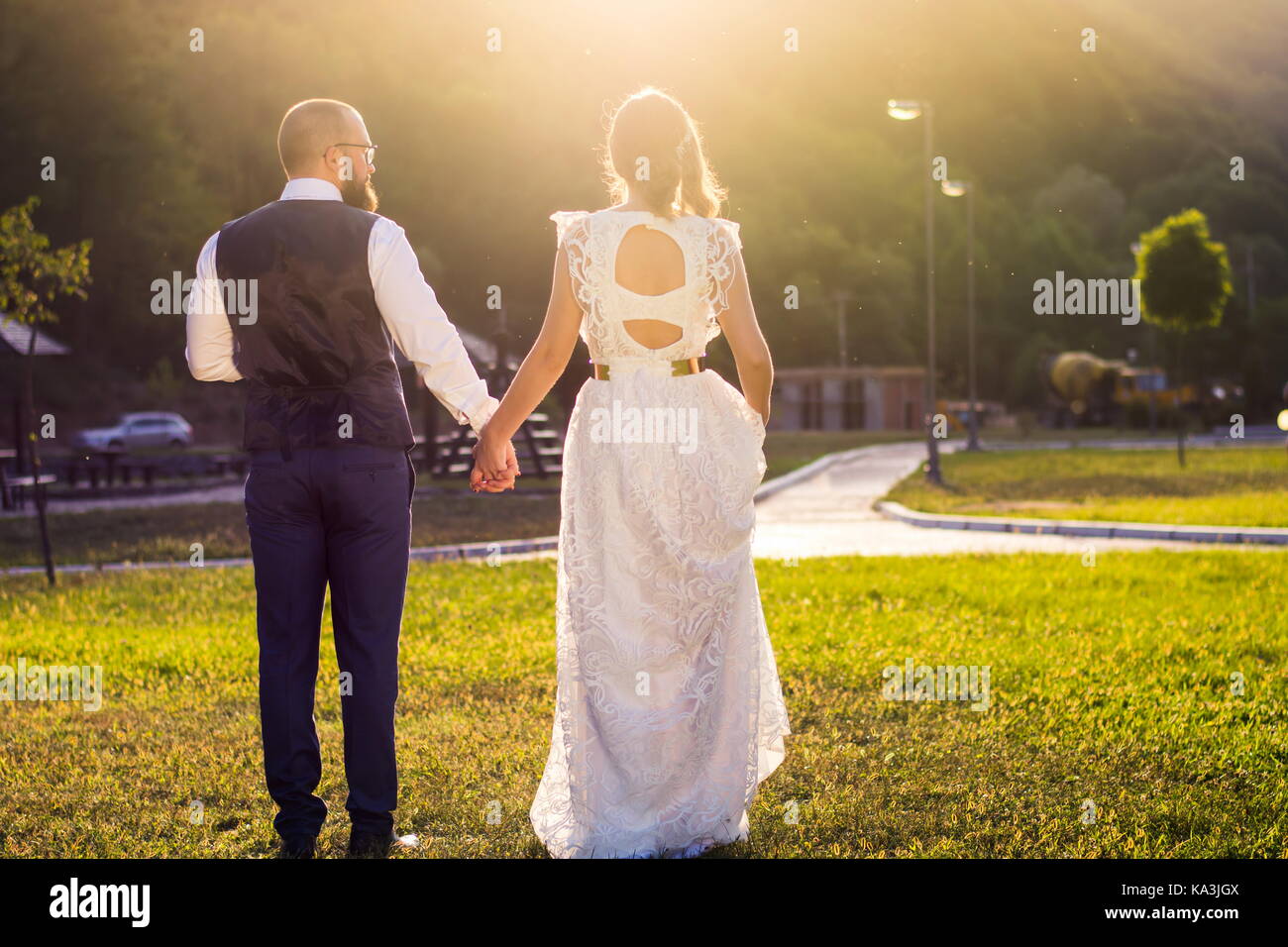 Mariée et le marié à marcher vers le coucher du soleil se tenant la main Banque D'Images