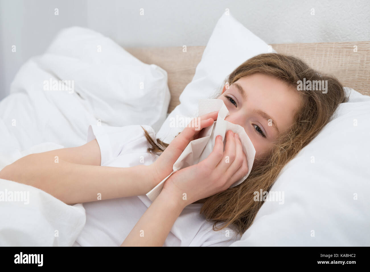 Sick Girl On Bed éternuer dans un mouchoir dans la chambre Banque D'Images
