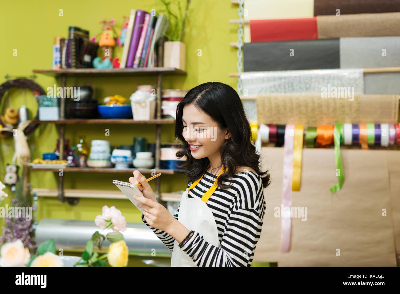 Smiling asian female florist prendre des notes au comptoir du magasin de fleurs Banque D'Images