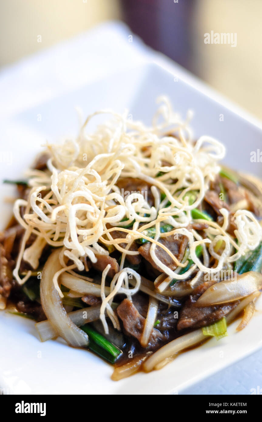 Sauté de boeuf mongole, sauté de boeuf aux oignons verts et blancs dans une sauce spéciale et surmontée de nouilles de riz croustillant. Banque D'Images