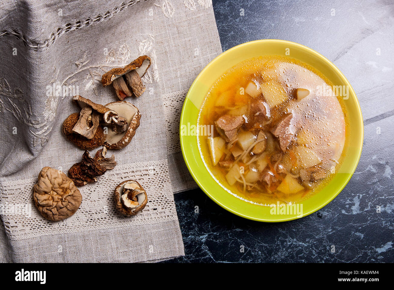 Soupe aux champignons en plaque verte sur un fond noir en noir. plusieurs porcini séchés ou blanc champignons sauvages sur tissu marron. Banque D'Images