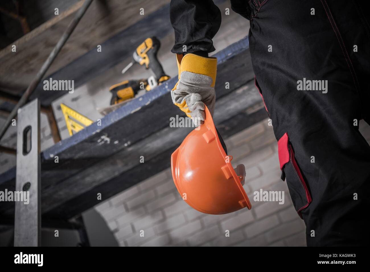 Casque de chantier avec l'entrepreneur. casque orange dans la main. échafaudages avec des outils en arrière-plan. Banque D'Images