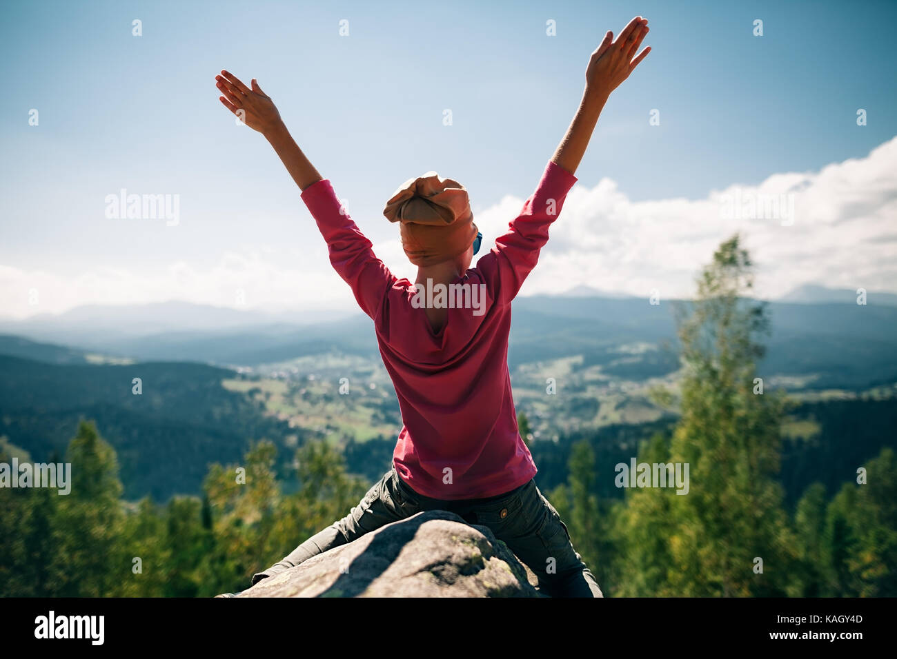 Heureux petite fille assise sur une falaise rocheuse dans la montagne avec les mains en l'enfance. Banque D'Images