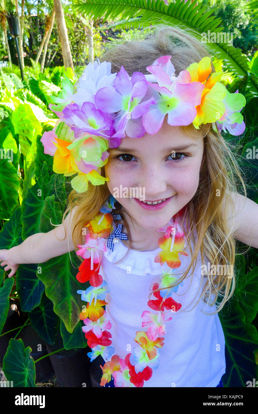 Enfant avec des cheveux longs et un sourire, vêtue d'une guirlande de fleurs hawaïennes colorées autour de la tête et du cou Banque D'Images
