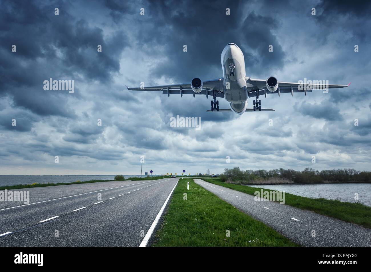 Route de l'avion et par temps couvert 24. Paysage avec grand avion de passagers est volant dans le ciel nuageux au-dessus de la route asphaltée et l'herbe. airlin passager Banque D'Images